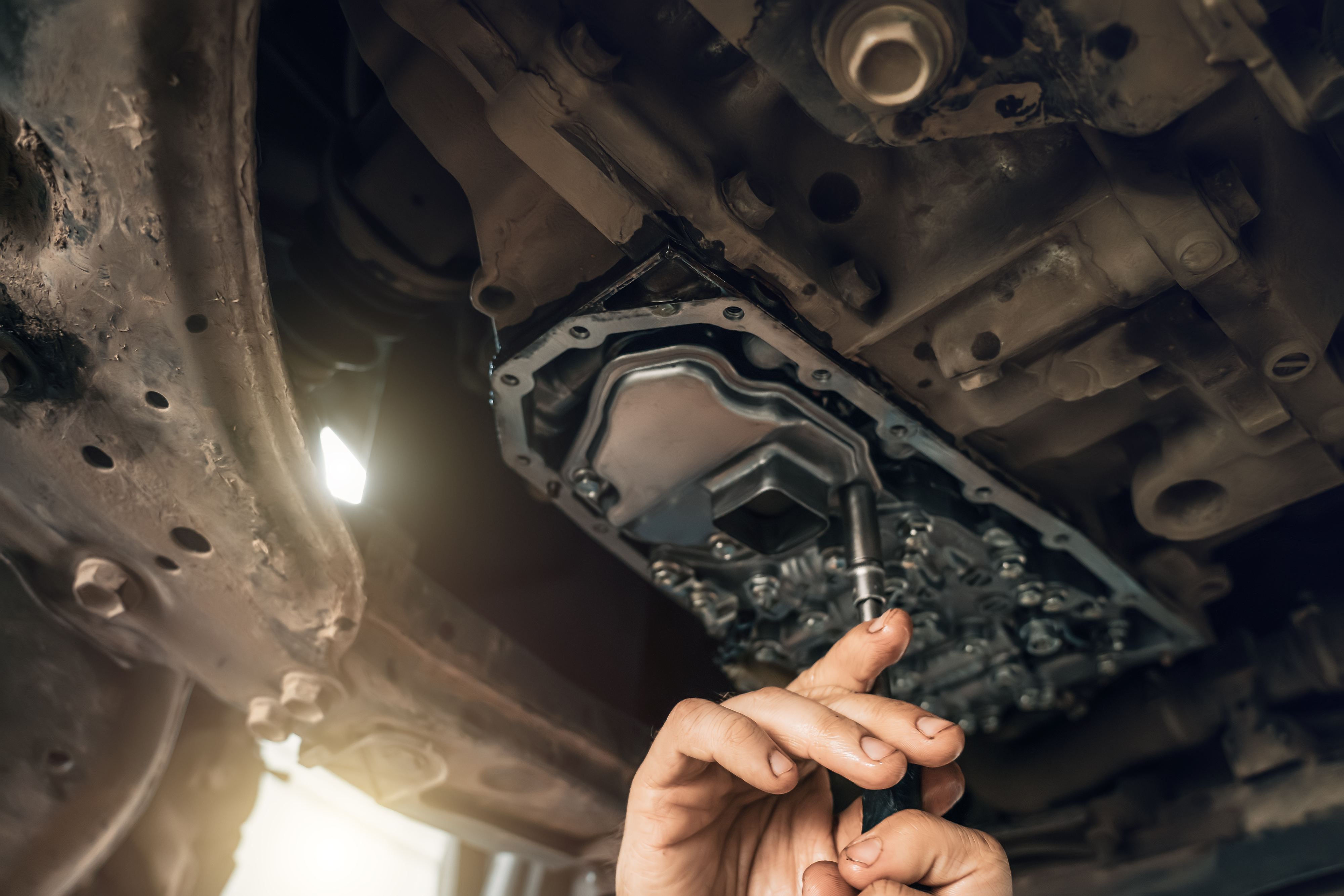 Mechanic working under vehicle inspecting transmission pan